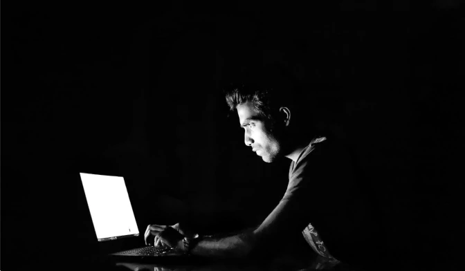 Bild eines Mannes vor einem Laptop in Dunkelheit