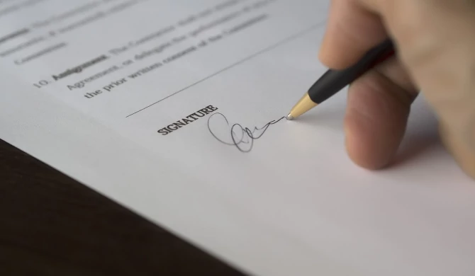Eine Hand, die mit einem Kugelschreiber auf einem Vertrag unterschreibt